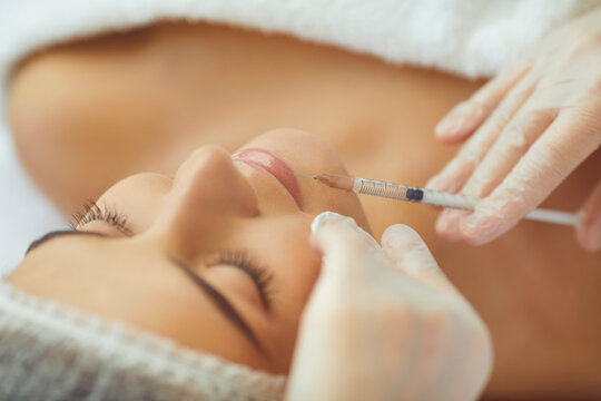 Cosmetologist making botox filler injection in female lips with syringe in beauty salon