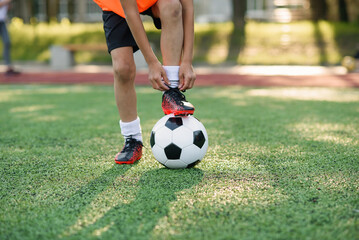Close up boot of football player which puts his leg on ball and tying shoelace on soccer stadium on the training.