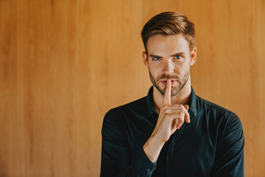 Young business man in classic shirt isolated on wooden background. Quiet with finger on lips shhh gesture