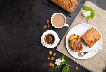 Homemade cake with raisins, almonds, soft caramel and a cup of coffee on a black concrete background. top view, copy space.