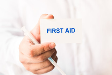 Word first aid on a white background with a syringe in hand. Medicine concept