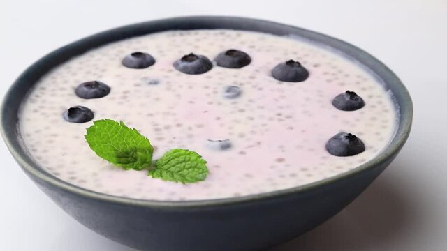 Rotating of yogurt with blueberry and chia in ceramic bowl on white background. Side view, close up.