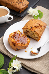 Homemade cake with raisins, almonds, soft caramel and a cup of coffee on a black concrete background. Side view, close up.