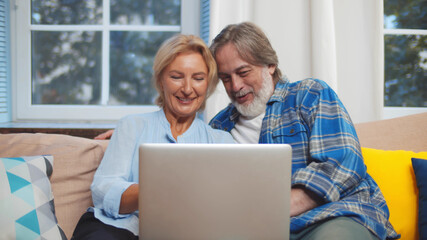 Senior couple relaxing and using laptop together sitting on sofa in living room at home