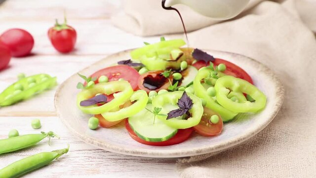Vegetarian salad from green pea, tomatoes, pepper and basil on white wooden background and linen textile poured with vinegar. Side view, close up.