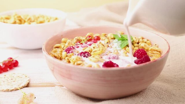 Wheat flakes porridge with raspberry and currant in ceramic bowl on white wooden background and linen textile poured with milk. Side view, close up.