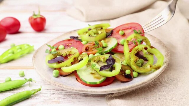 Vegetarian salad from green pea, tomatoes, pepper and basil on white wooden background and linen textile stir with a fork. Side view, close up.