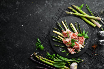 Prosciutto with boiled asparagus and spices on a black stone plate. Top view. Free space for your text. - obrazy, fototapety, plakaty