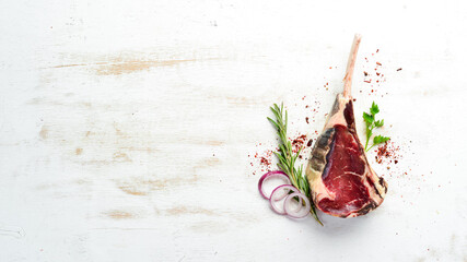 Fototapeta na wymiar Raw dry steak on bone. Tomahawk steak on a white wooden background. Top view. Free space for your text.
