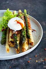 Breakfast of baked asparagus in spices with bacon, poached egg and crispy salad. Side dish for lunch, dinner.