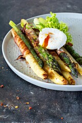 Breakfast of baked asparagus in spices with bacon, poached egg and crispy salad. Side dish for lunch, dinner.