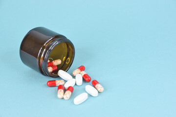 Overturned glass jar with scattered red and white pills on blue background