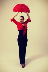 woman in black pants and red bullfighter dancing sevillanas flamenco with red fan