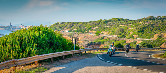 Bikers riding on a winding road with Alghero on the background