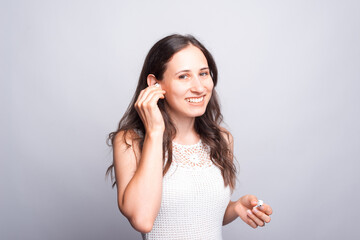 happy and smiling woman using earpods and looking confident at the camera over white wall