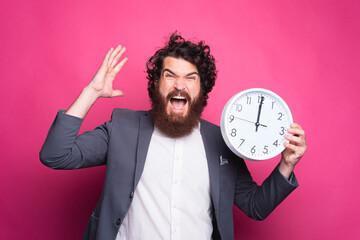 Portrait of angry business man screaming and holding CLOCK, delay concept