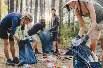 Group of young friends volunteers with trash bags in forest, helping to clean forest from litter.