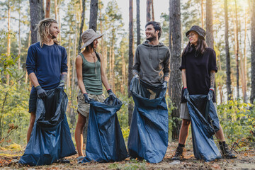 Portrait of happy young eco volunteers picking plastic from forest while standing with bags together