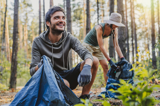 Cheerful Mixed Race Man Looking Away While Collecting Trash With Friends Outdoor