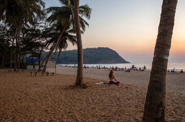 a girl with red hair in a bikini sits on the beaches in the lotus position (yoga) and watches the sunset from the sun.