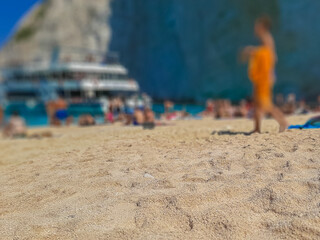 Fototapeta na wymiar Sand foreground with blurred people and yacht in the background, Zakynthos island, Greece
