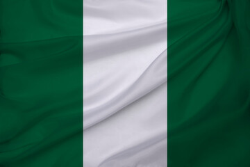 Obraz premium photo of the national flag of Nigeria on a luxurious texture of satin, silk with waves, folds and highlights, closeup, copy space, travel concept, economy