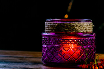 Purple lantern, orange golden nugget pumpkin rowan berries and two candles on wooden rustic table and black background with yellow bokeh dots, autumnal warm mood in cozy home decoration.