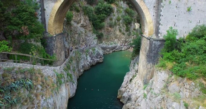 Tilt down aerial, man jumps into water under Furore Bridge