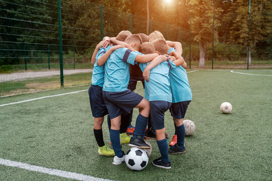 Children soccer team and coach hugs each other on football field before match