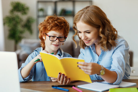 Mother helping child with homework, looks at her son's notebook at home.