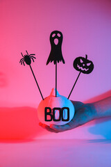 Halloween home decorations. A human hand holds a painted white pumpkin and black scary Halloween...