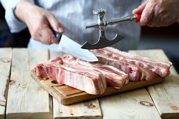 The chef cuts raw pork ribs with a hatchet. Cooking meat. Selective focus. Macro.