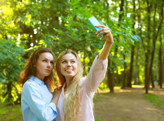 Obraz premium mature mother and adult daughter are doing selfie by mobile phone in summer park
