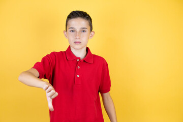 Young beautiful child boy over isolated yellow background with angry face, negative sign showing dislike with thumb down