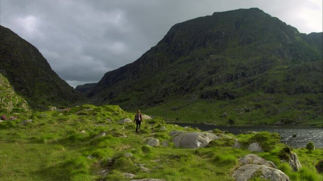Wide aerial, woman hikes through Irish countryside