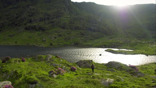 Panning aerial, woman walks along lake in Ireland mountains