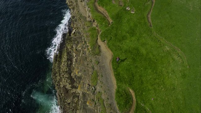 Overhead aerial, person hikes along Ireland cliffs