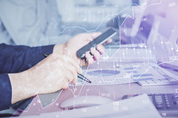 Double exposure of man's hands holding and using a digital device and forex graph drawing. Financial market concept.