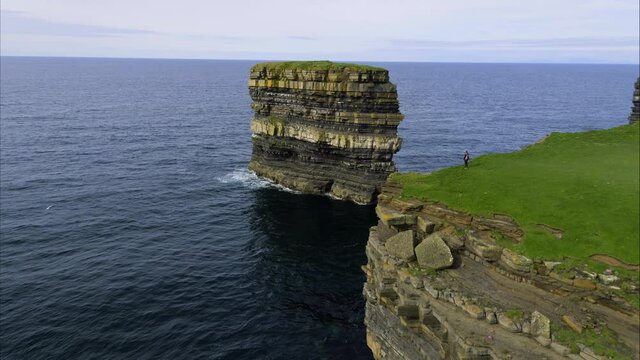 Person walks along Ireland coastal cliffs, panning aerial