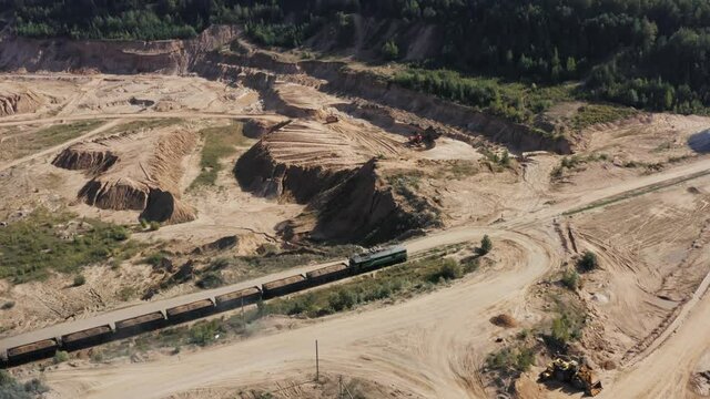 Aerial view sand quarry, industrial extraction of sand for construction industry. Drone flies over freight train, excavator loading stone and rock into dump truck. Mining truck transporting sand
