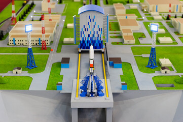 Spaceport scale model with spaceship on launch platform, layout of rocket ready to start with floodlights, buildings and roads on blurred background, aerospace industry, selective focus