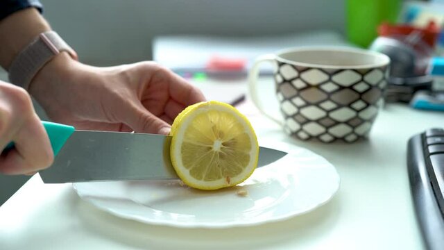 Women's hands cut a lemon on a white plate in office Horizontal, fingers, knife, reamer. Lady hands closeup