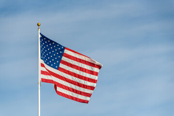 American flag blowing in the wind at sunset, against a blue sky with wispy white clouds
