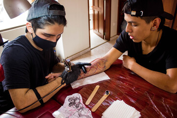 High angle shot of a young male tattoo artist with gloves and a facemask tattooing a customer