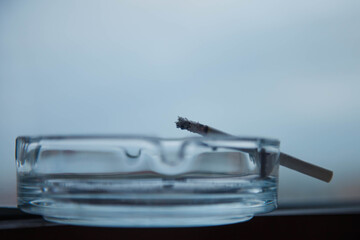 Close-up of an ashtray with Smoking cigarette on neutral blue-gray background. Concept of the harm of Smoking tobacco or Smoking cigarettes in public places. Copyright space for site or banner