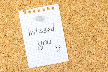 Note on a sheet from a notebook ?missed you? and a painted sad face pinned to a corkboard