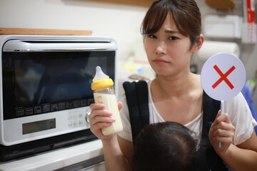 電子レンジの前でミルクと×の札を持つ母親