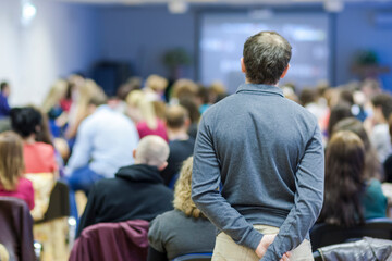 Back View of A Man Standing Behind A Large Group of People Attending Conference.