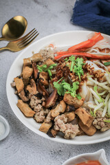 Chinese Steamed Rice Noodles with pork ,sausage,imitation Crab Stick,boil bean sprouts,mushroom and tofu in sweet soy sauce in white plate.Chili powder,pickled chili and sugar on table .
