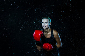 Female Boxer  Posing with Red Gloves In Water Droplets Against Black Background.